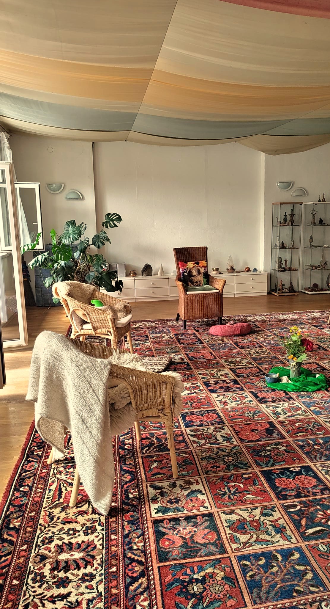 Blick in einen großen, weitläufigen und sonnigen Raum mit Perserteppichen, Korbstüheln und über die Decke gespannten Tüchern